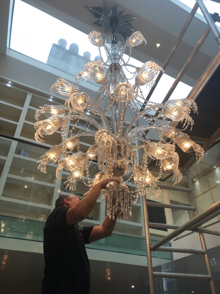 a memeber of the elite team giving a chandelier clean hir full attention 